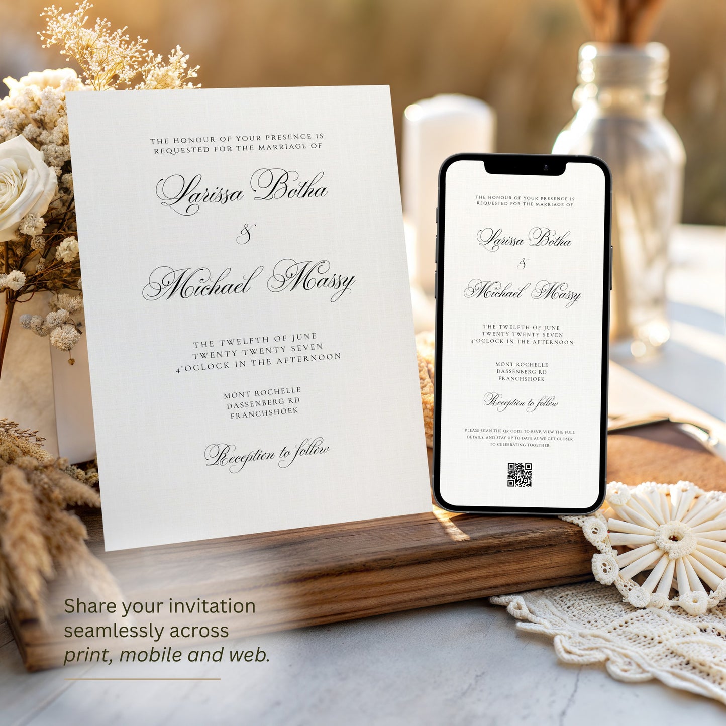 A ivory wedding invitation card and a smartphone displaying the same invitation design, styled on a wooden tray with dried flowers, a glass bottle, and lace in a warm indoor setting.