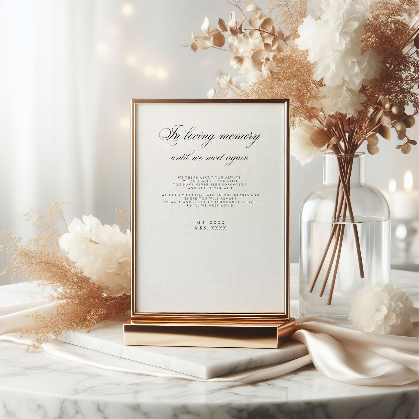 A framed wedding memorial sign with elegant black script and block text, displayed on a marble surface with satin fabric, dried flowers, and a glass vase in a softly lit setting.