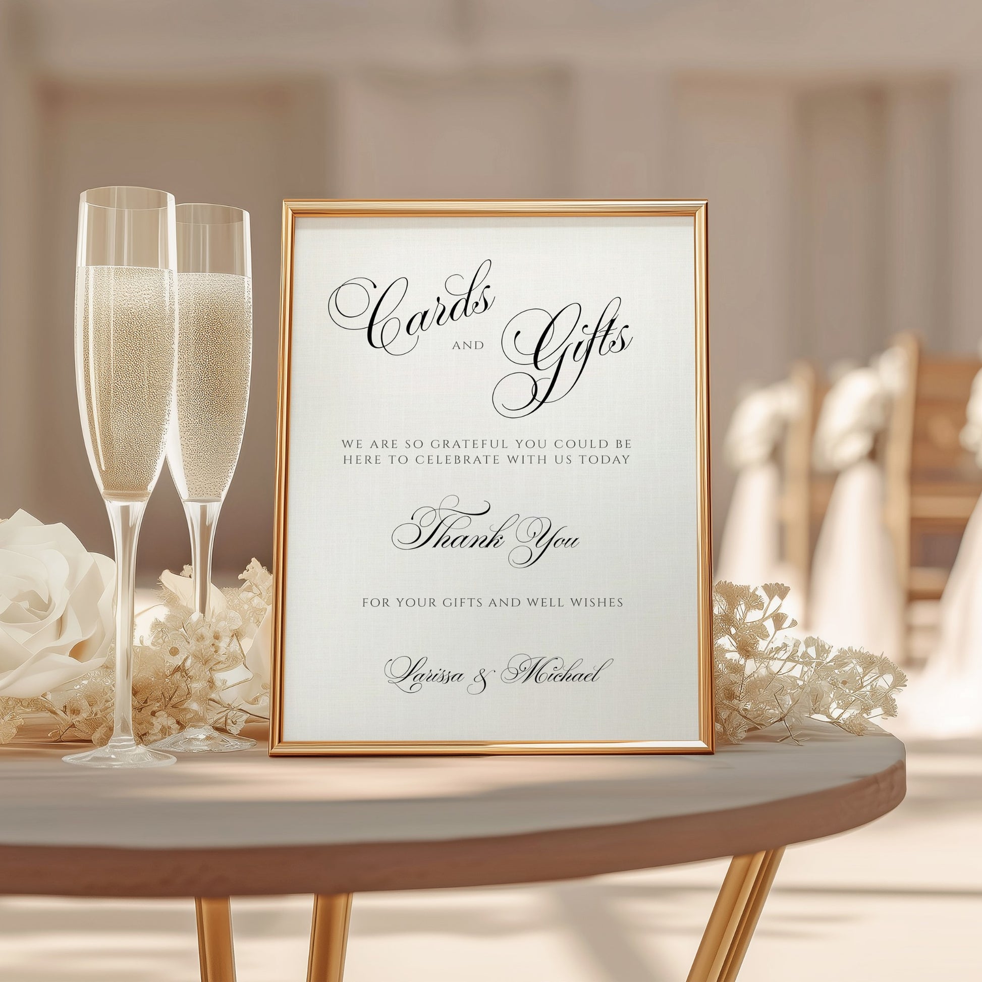 A framed wedding cards and gifts sign with elegant black script on a cream background, styled on a round table with champagne flutes, flowers, and a softly blurred wedding venue in the background.